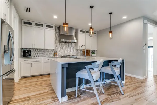 a kitchen with stainless steel appliances granite countertop a sink a stove a refrigerator and chairs with wooden floor
