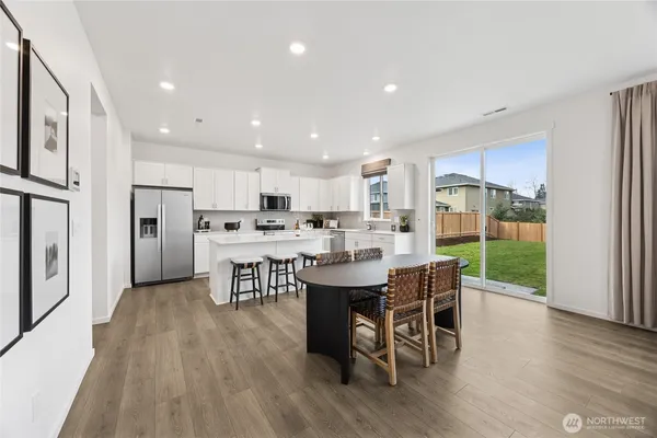 a open kitchen with stainless steel appliances granite countertop a dining table chairs refrigerator sink and cabinets