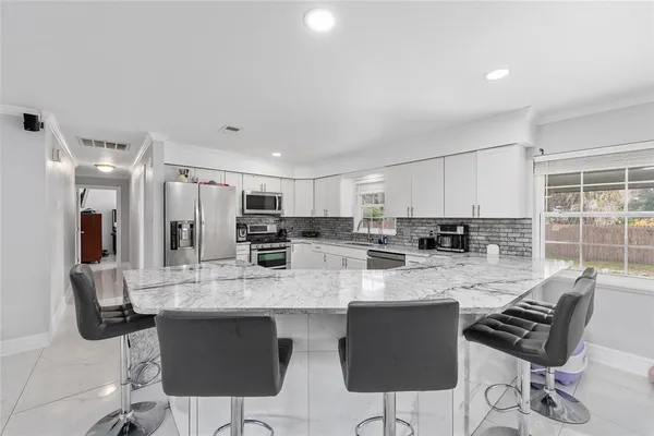 a kitchen with stainless steel appliances kitchen island granite countertop a stove a sink a refrigerator white cabinets and chairs