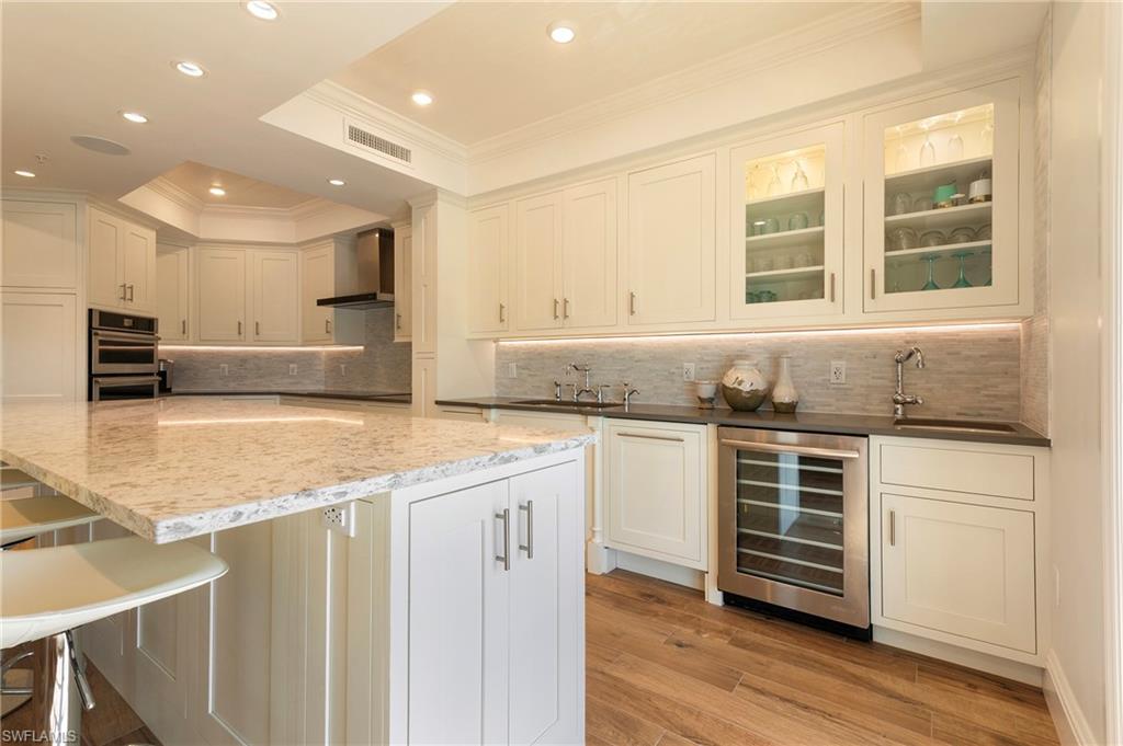 451 Bayfront Place, Unit 5407 Naples, FL 34102 - Photo 13 of 38 Bar area featuring white cabinetry, light wood-type flooring, beverage cooler, crown molding, and glass fronted cabinets
