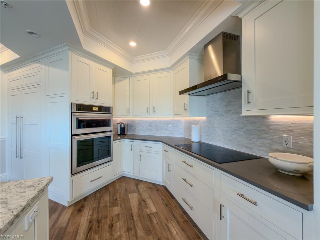 451 Bayfront Place, Unit 5407 Naples, FL 34102 - Photo 6 of 45 Kitchen with dark wood finished floors, white cabinets, stainless steel double oven, ornamental molding, and backsplash