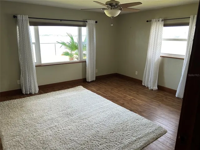 an empty room with wooden floor fan and windows