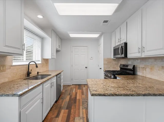 a kitchen with granite countertop kitchen island a sink stainless steel appliances and white cabinets