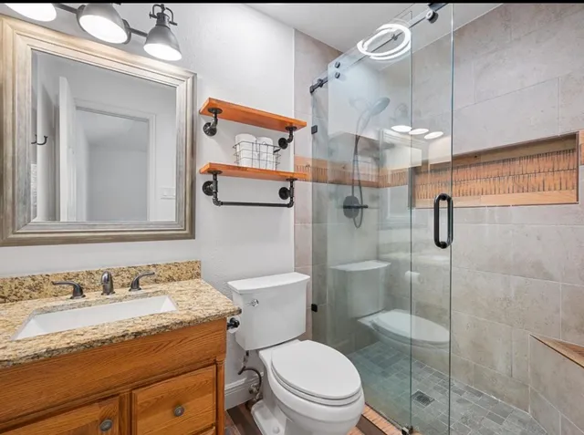 a bathroom with a granite countertop sink vanity mirror and toilet