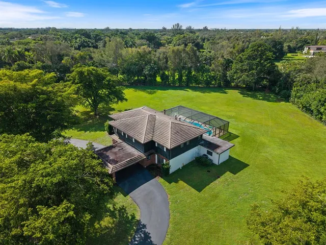 an aerial view of a house with pool big yard and large trees