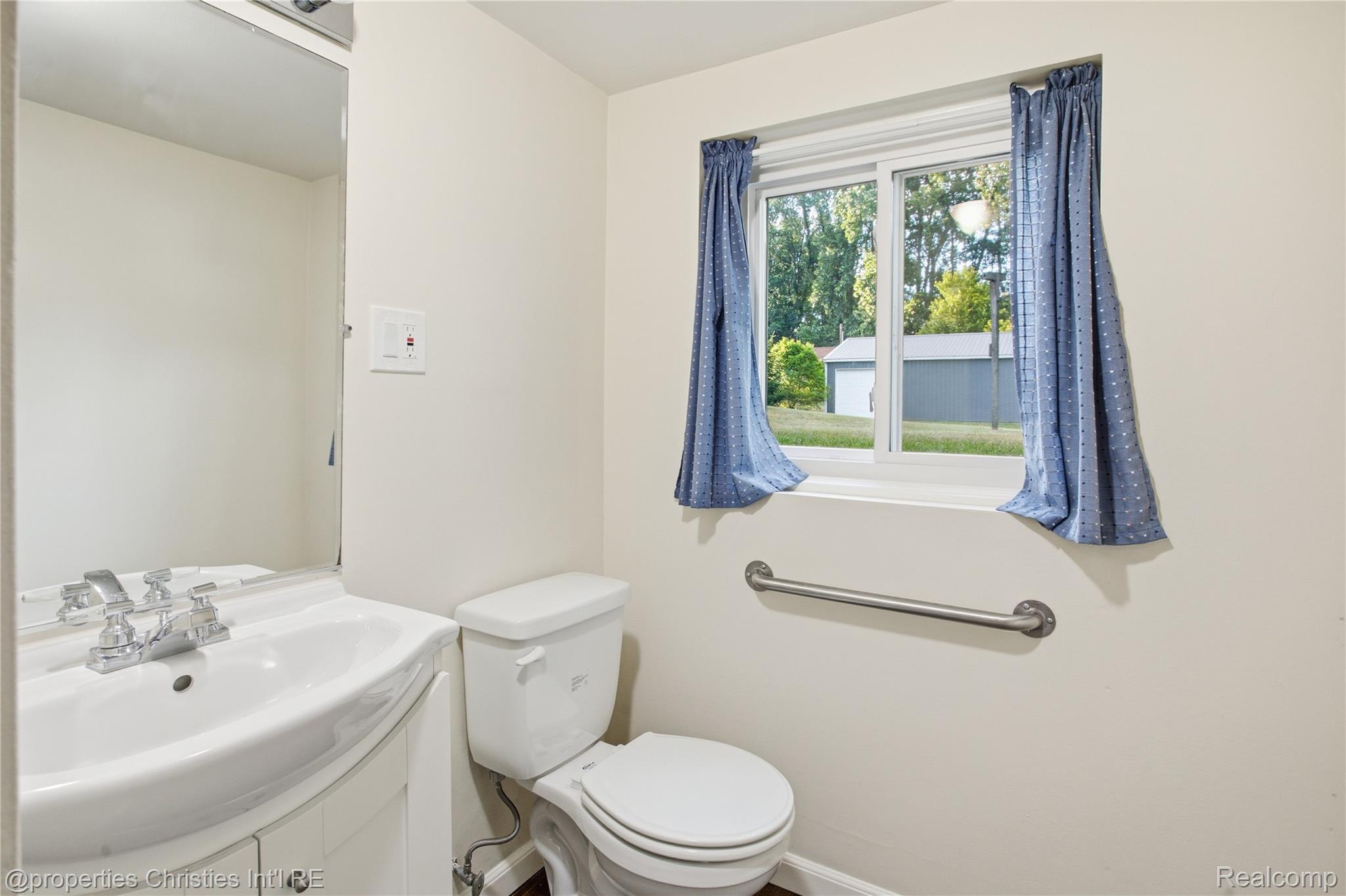3851 Judd Road Milan, MI 48160 - Photo 26 of 41 Bathroom featuring a single-pane window, white toilet, wall-mounted grab bar, pedestal-style sink with a chrome faucet, and a wall mirror