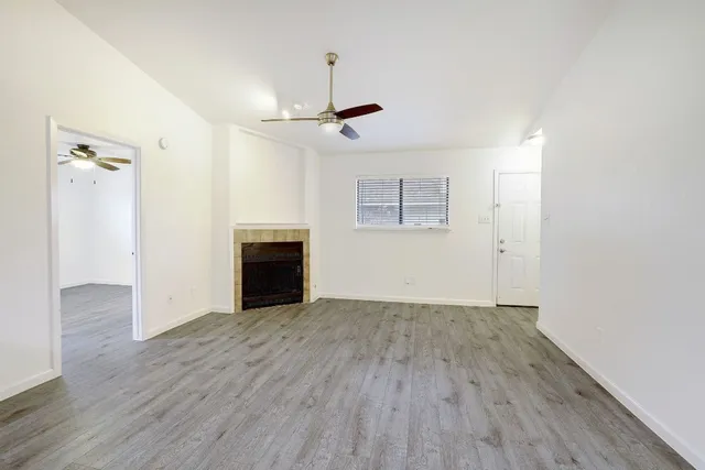 an empty room with wooden floor chandelier fan and windows