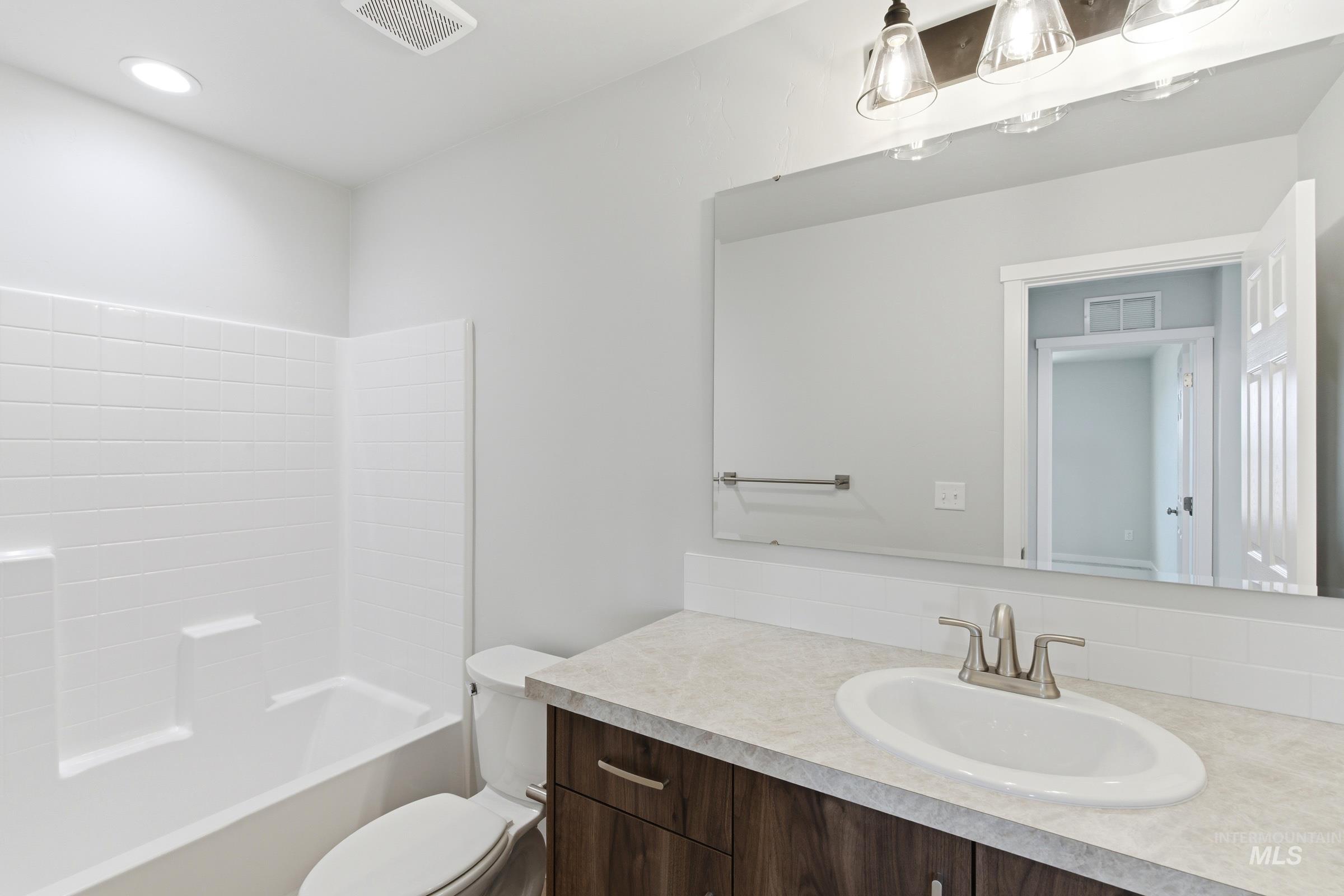 16558 Dunning Way Caldwell, ID 83607 - Photo 32 of 35 Full bathroom featuring a white subway tile tub surround, a wood-finish vanity with a light-toned countertop, and an oval undermount sink