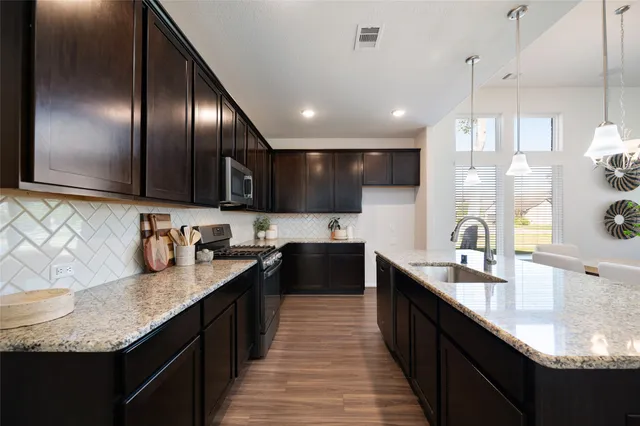 a kitchen with stainless steel appliances kitchen island granite countertop a large stove top oven a sink dishwasher and wooden cabinets with wooden floor