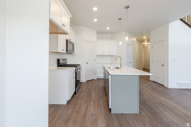 4816 Heartwood Road, Unit 423 Mapleton, UT 84664 - Photo 8 of 21 Dual tone kitchen with stainless steel appliances, two tone cabinetry, dark wood-style floors, a kitchen island with sink, and decorative light fixtures