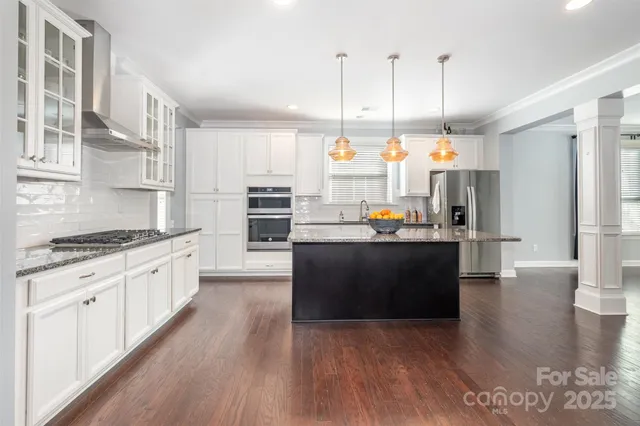 a kitchen with stainless steel appliances kitchen island granite countertop a refrigerator a stove and a wooden floors