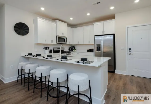 a kitchen with stainless steel appliances granite countertop a dining table chairs refrigerator and cabinets