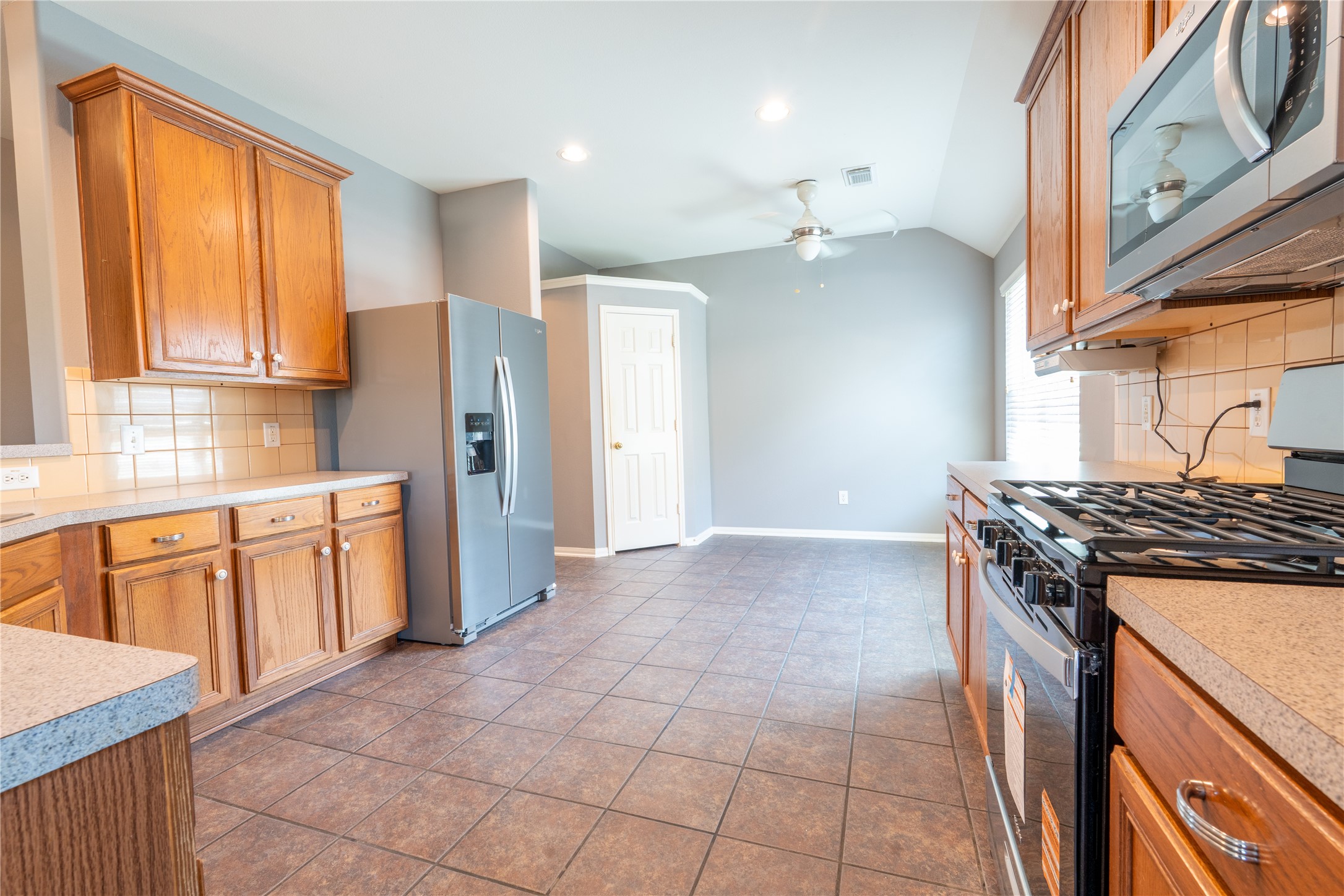 10619 Crownsedge Drive Spring, TX 77379 - Photo 7 of 38 The kitchen offers a modern stainless steel refrigerator and gas stove. It has tiled flooring, ample counter space, and a ceiling fan, offering a functional and bright cooking area.