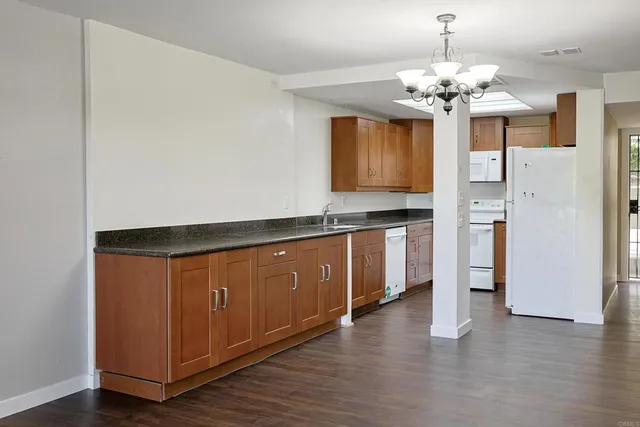 a kitchen with stainless steel appliances granite countertop a refrigerator a sink dishwasher a oven and a dining table with wooden floor