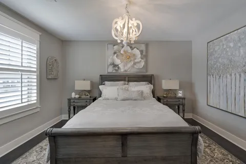 a large bed sitting in a bedroom next to a window with a chandelier and a chair