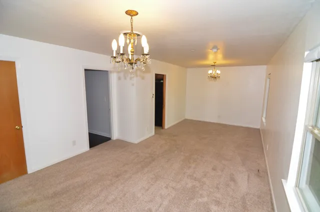 an empty room with chandelier fan and windows