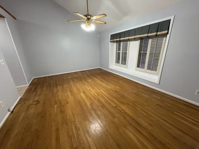 a view of an empty room with wooden floor and fan
