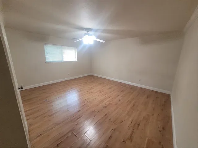 an empty room with wooden floor fan and windows