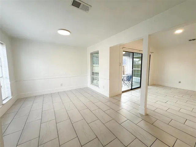 an empty room with windows and way to kitchen