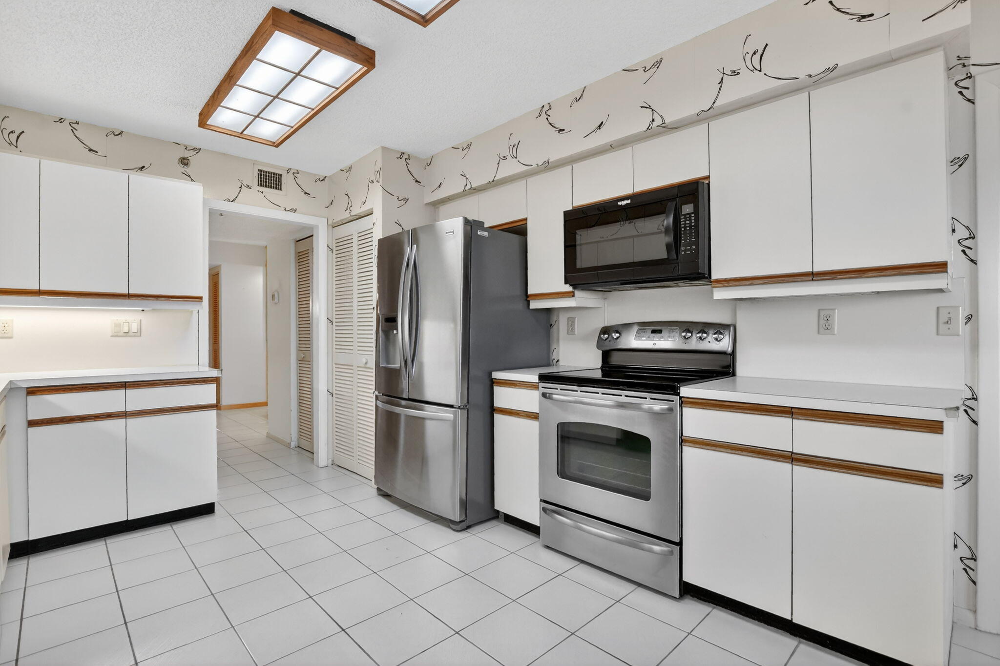 7564 Regency Lake Drive, Unit 701 Boca Raton, FL 33433 - Photo 20 of 47 a kitchen with white cabinets stainless steel appliances and a window