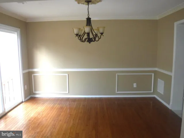 a view of an empty room with chandelier fan and wooden floor