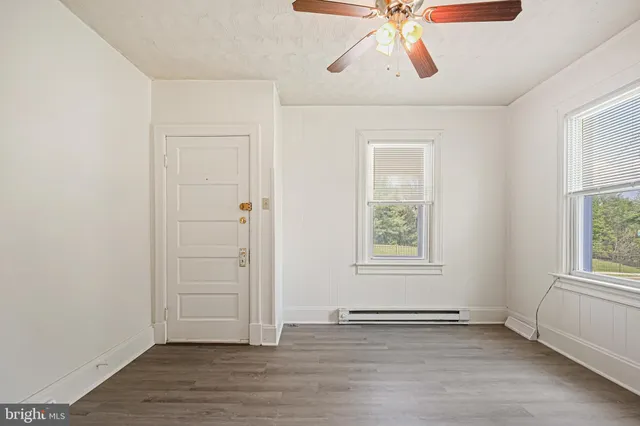 an empty room with wooden floor chandelier fan and windows