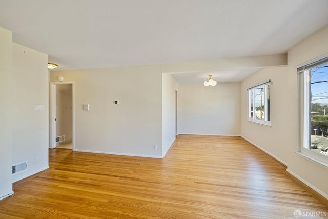 a view of an empty room with window and wooden floor