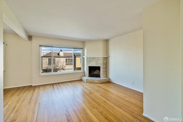 an empty room with wooden floor fireplace and windows