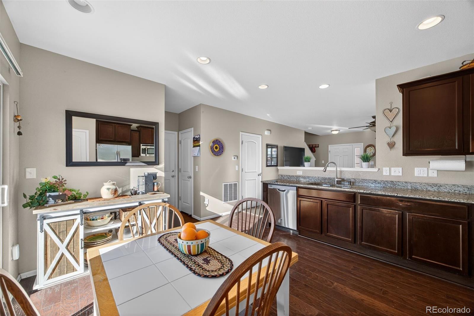 10247 Olathe Way Commerce City, CO 80022 - Photo 13 of 37 a kitchen with stainless steel appliances granite countertop a stove top oven a sink dishwasher a dining table and chairs with wooden floor