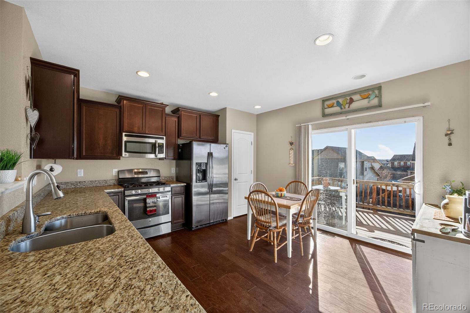 10247 Olathe Way Commerce City, CO 80022 - Photo 10 of 37 a kitchen with stainless steel appliances granite countertop a stove top oven a sink a dining table and chairs with wooden floor