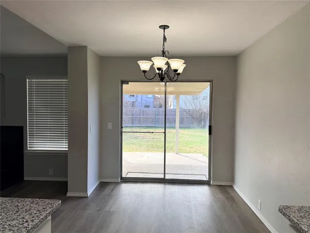 a view of an empty room with wooden floor kitchen view and a window