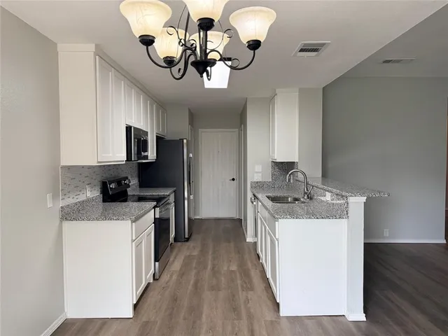 a kitchen with a sink a chandelier stainless steel appliances and cabinets