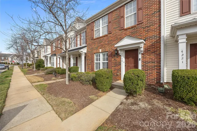 a view of a brick house with plants and large tree