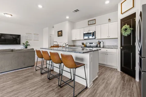 a kitchen with stainless steel appliances kitchen island granite countertop a stove a sink a microwave a dining table and chairs with wooden floor