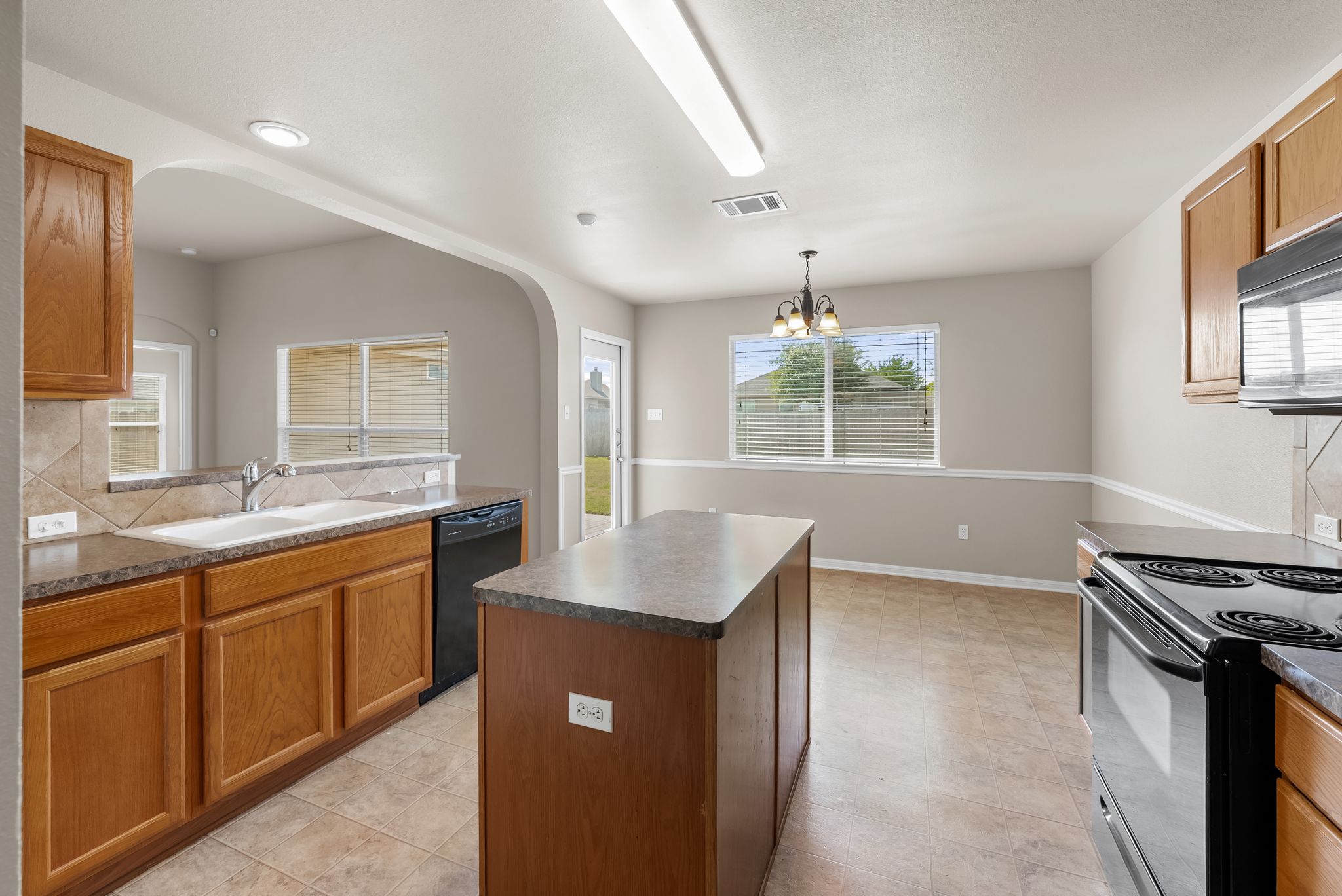 7719 Fieldstone Drive Temple, TX 76502 - Photo 20 of 37 Kitchen featuring black appliances, wood finish cabinetry, a center island, decorative backsplash, and dark countertops