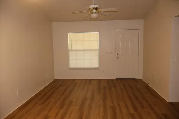an empty room with wooden floor chandelier fan and windows
