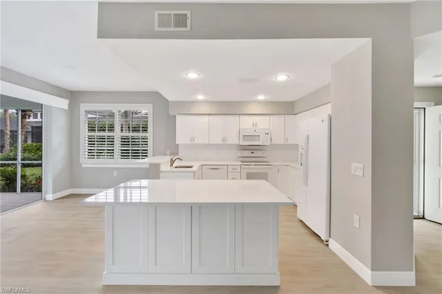 a large white kitchen with kitchen island a large window appliances and a counter top space