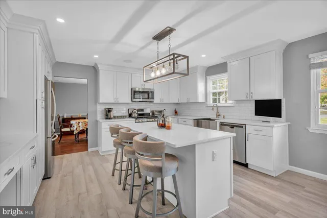 a kitchen with stainless steel appliances a stove a sink dishwasher a refrigerator white cabinets and wooden floor