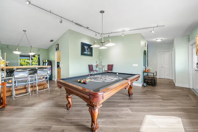 a room with wooden floor pool table and chairs