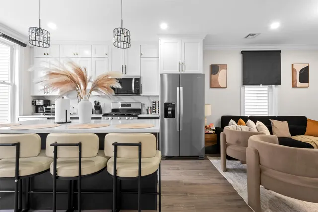 a kitchen with stainless steel appliances kitchen island granite countertop a refrigerator a sink dishwasher a dining table and chairs with wooden floor