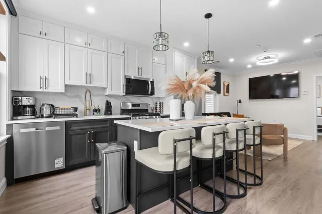 a kitchen with stainless steel appliances kitchen island granite countertop a sink a stove a dining table and chairs with wooden floor