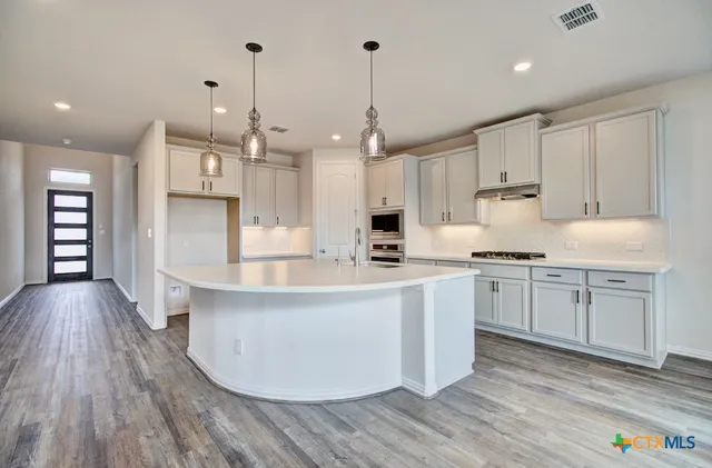 a large kitchen with kitchen island a stove a sink dishwasher and a oven with white cabinets