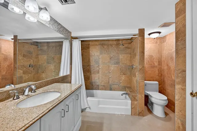 a bathroom with a granite countertop sink a toilet a mirror a bathtub and shower