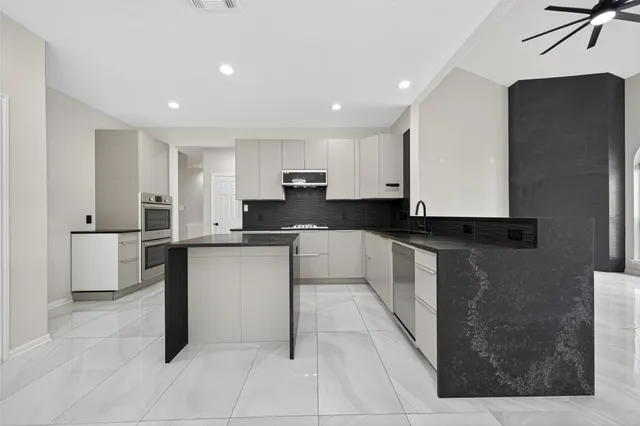 a large kitchen with stainless steel appliances kitchen island granite countertop a refrigerator a sink and white cabinets