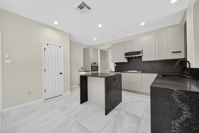 a kitchen with granite countertop a refrigerator a sink and white cabinets