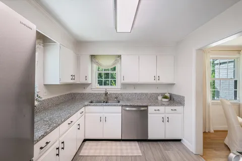 a kitchen with a sink dishwasher a stove and white cabinets with wooden floor