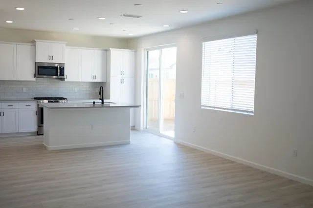 a large kitchen with stainless steel appliances granite countertop a stove a sink and white cabinets with wooden floor