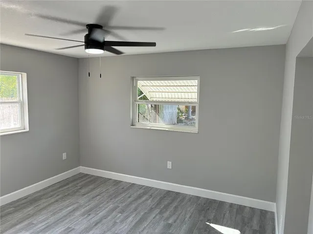 an empty room with wooden floor fan and windows