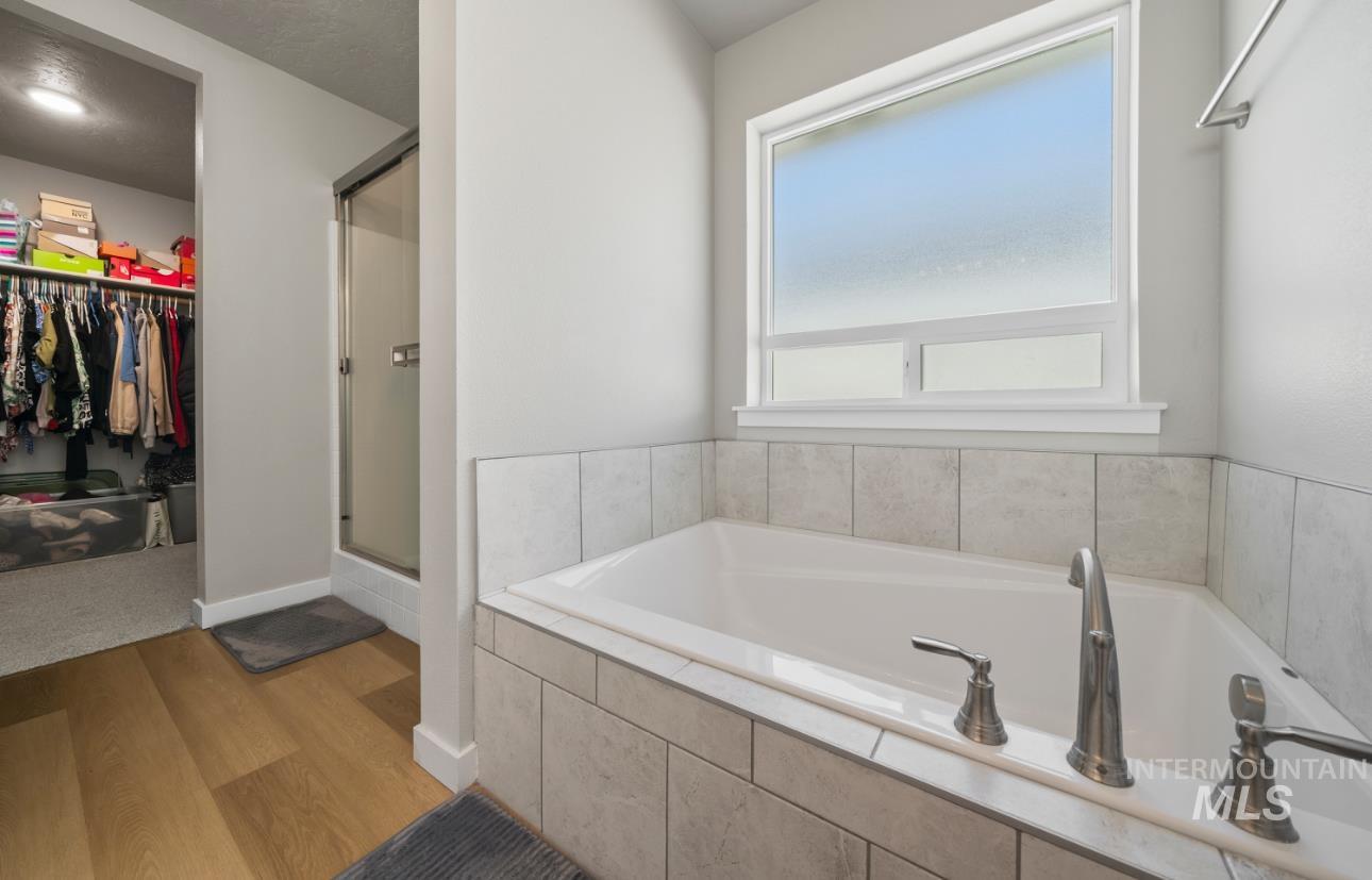 12443 Varga Street Caldwell, ID 83607 - Photo 16 of 27 Full bath featuring wood finished floors, a stall shower, a walk in closet, and a bath