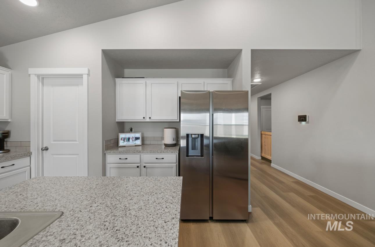 12443 Varga Street Caldwell, ID 83607 - Photo 5 of 27 Kitchen with stainless steel fridge with ice dispenser, light wood-type flooring, white cabinetry, vaulted ceiling, and light stone counters